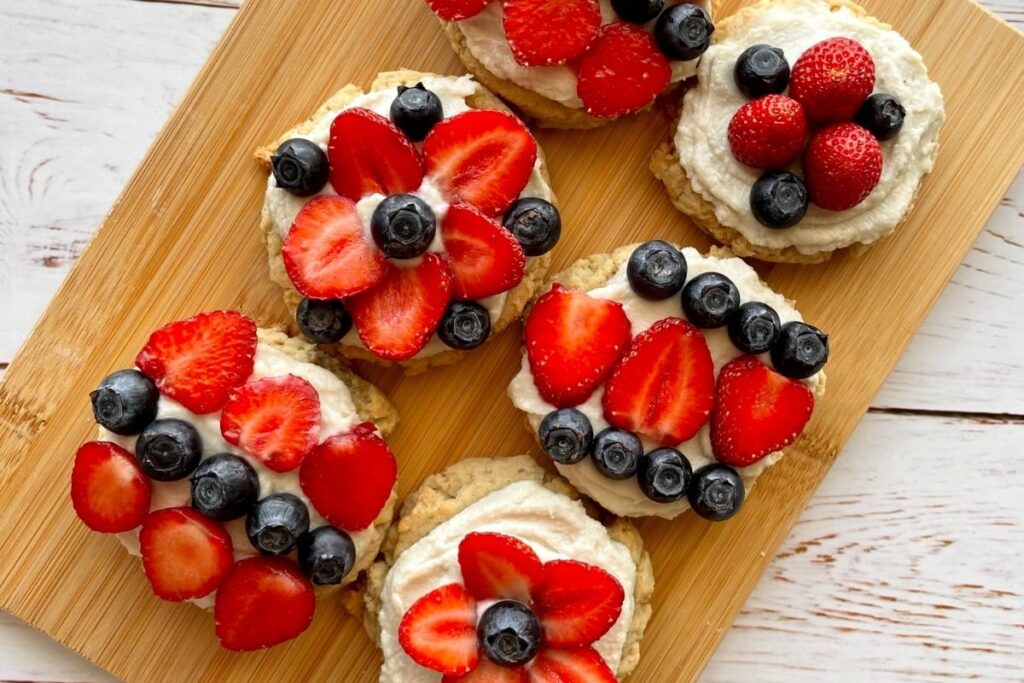 frosted cookies with strawberries and blueberries on a cutting board