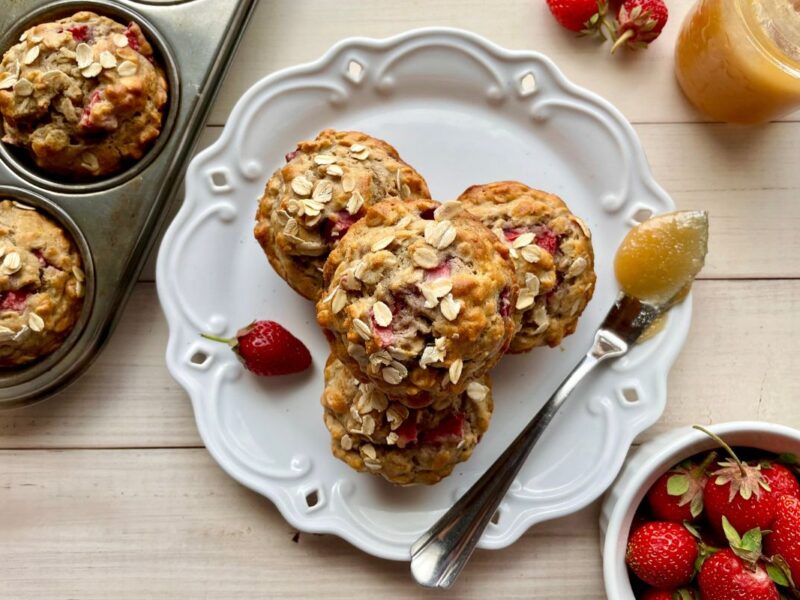 strawberry banana oatmeal muffins on a plate with fresh strawberries and honey