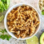 bowl of sweet pork with lettuce, lime, rice, avocado, cilantro in background