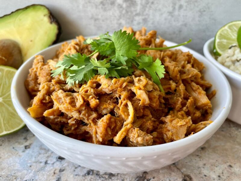 bowl of sweet pork with cilantro on top, cilantro lime brown rice, avocado and lime in back